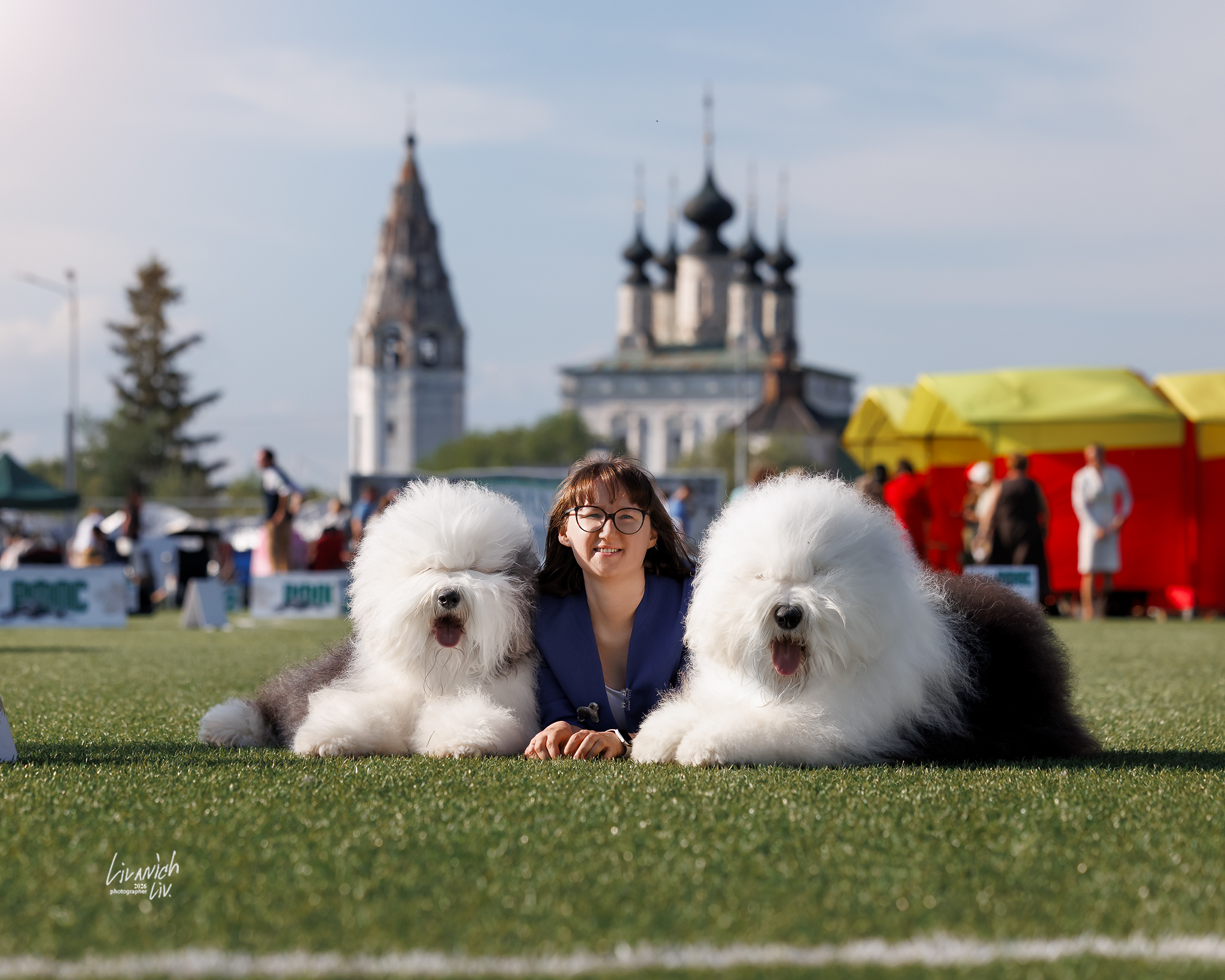 Woman posing with two Old English Sheepdogs at a dog show